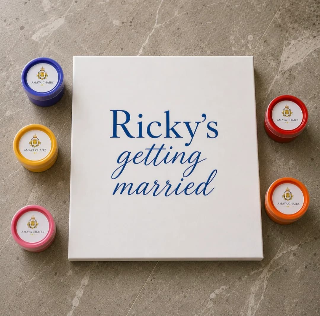 A personalised Maiyan board reading “Ricky’s getting married” in blue lettering, ringed by coloured rangoli powder pots.