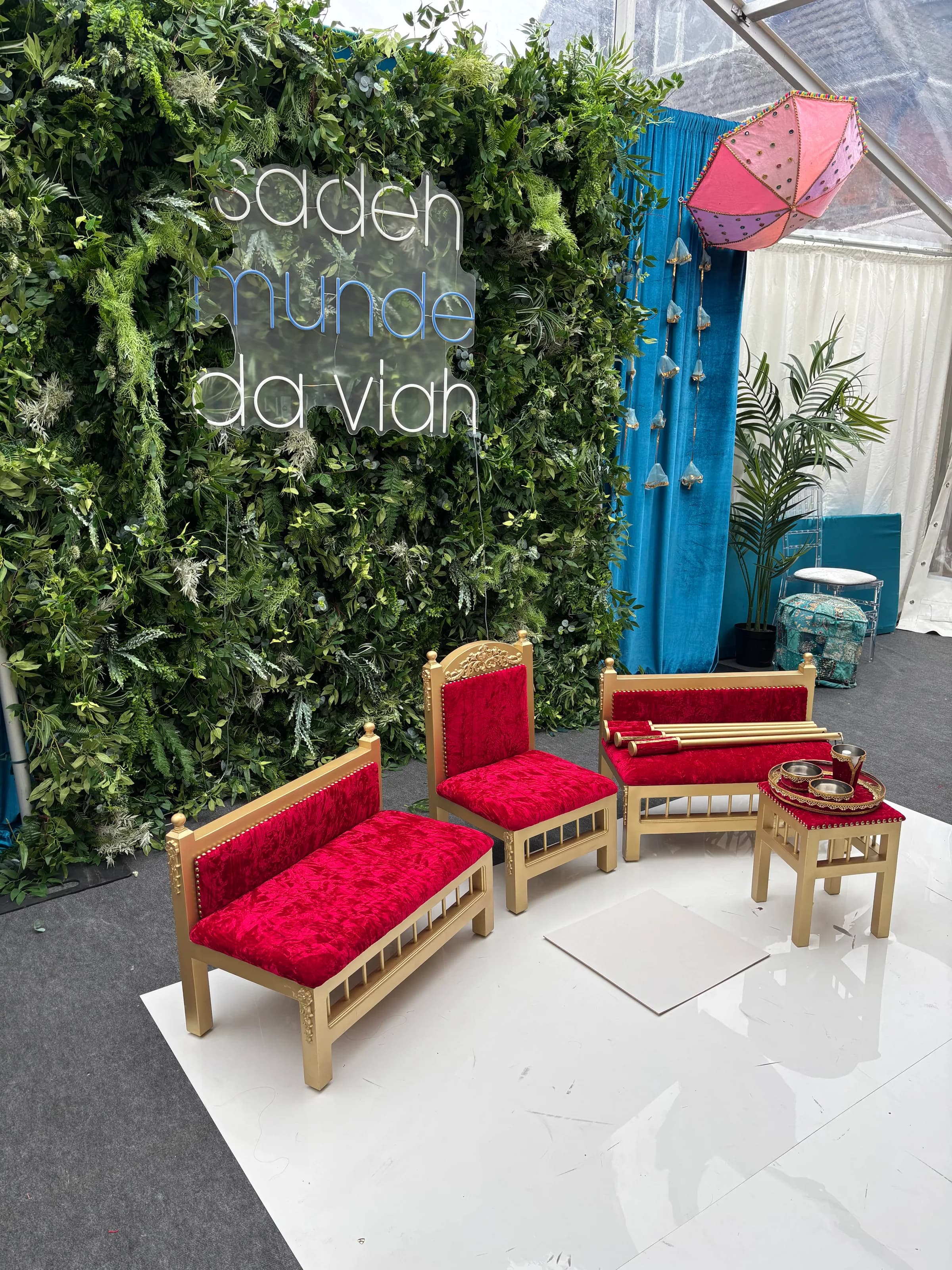 The Royal Crimson suite at a real Maiyan in front of a foliage wall with an illuminated Punjabi neon sign.