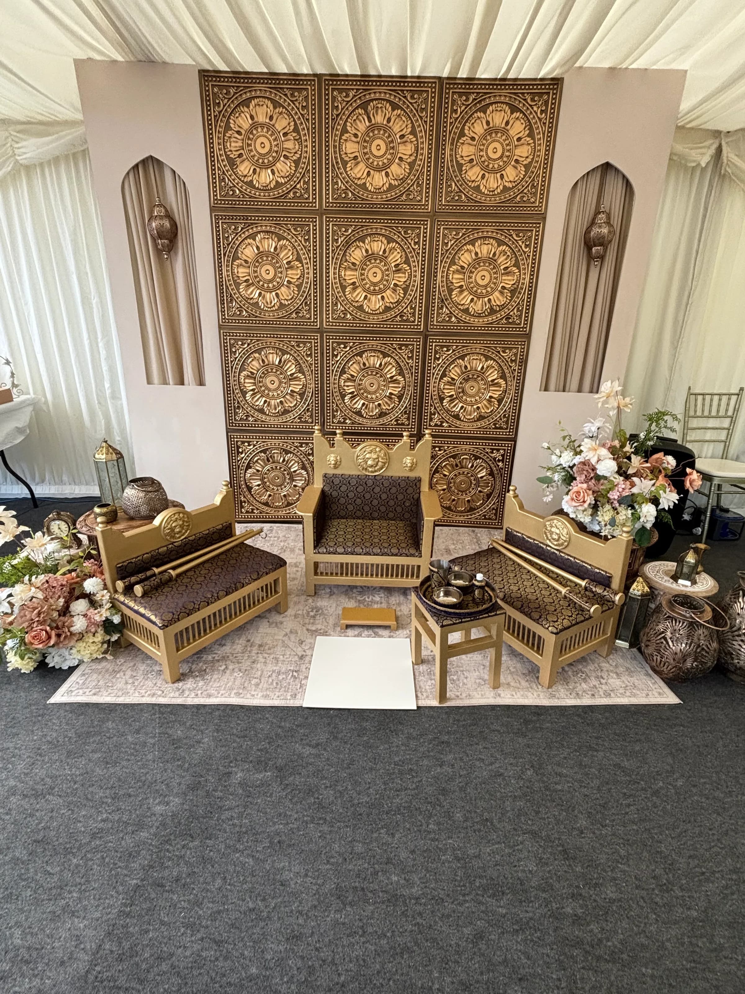 The Majestic Lion suite styled inside a marquee at a real event, set in front of a carved gold screen with floral arrangements on either side.