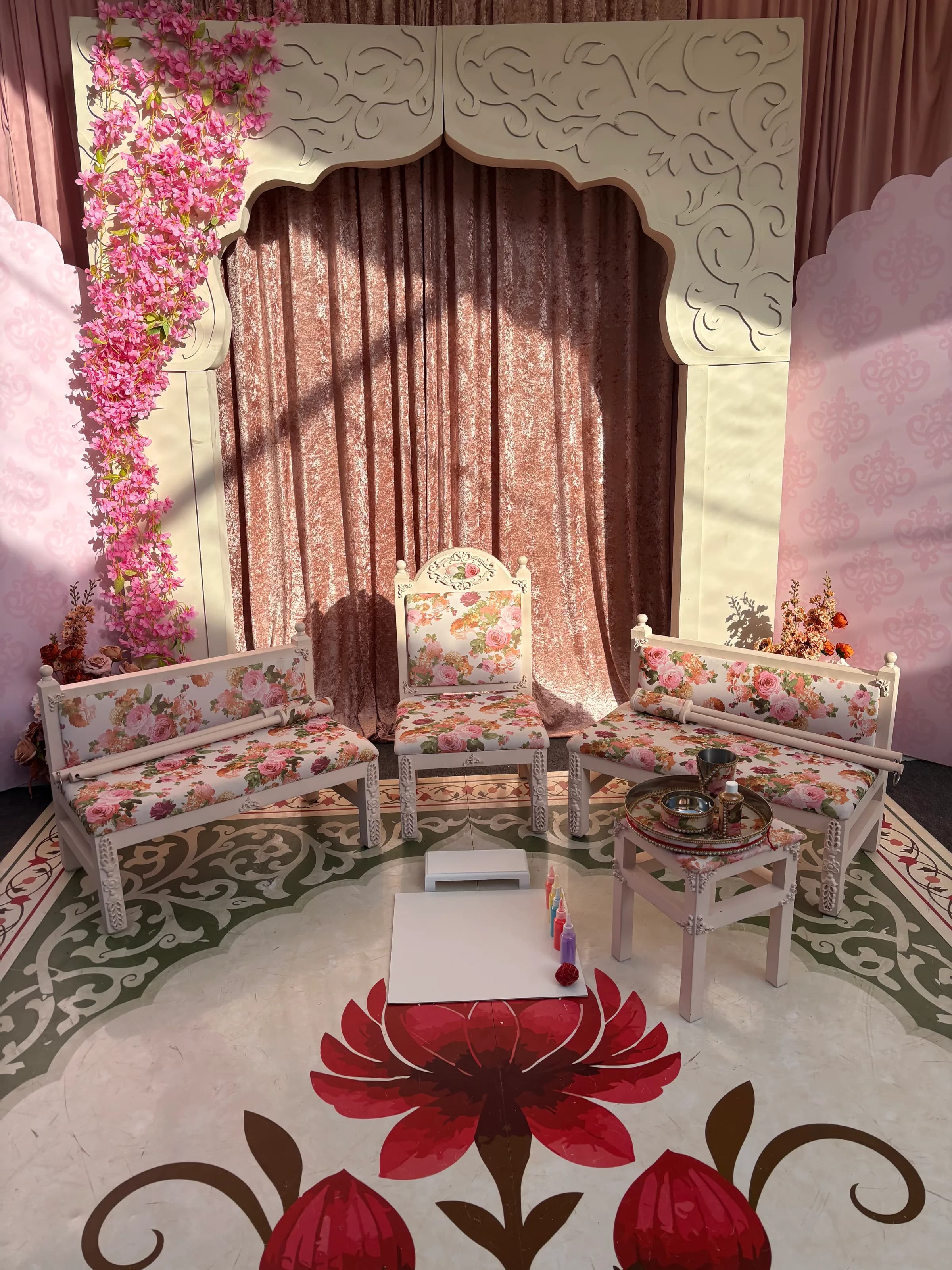 The Enchantress suite set for a ceremony beneath a cascade of pink blossom, with rose-gold drapes behind and a lotus rangoli laid on the floor.