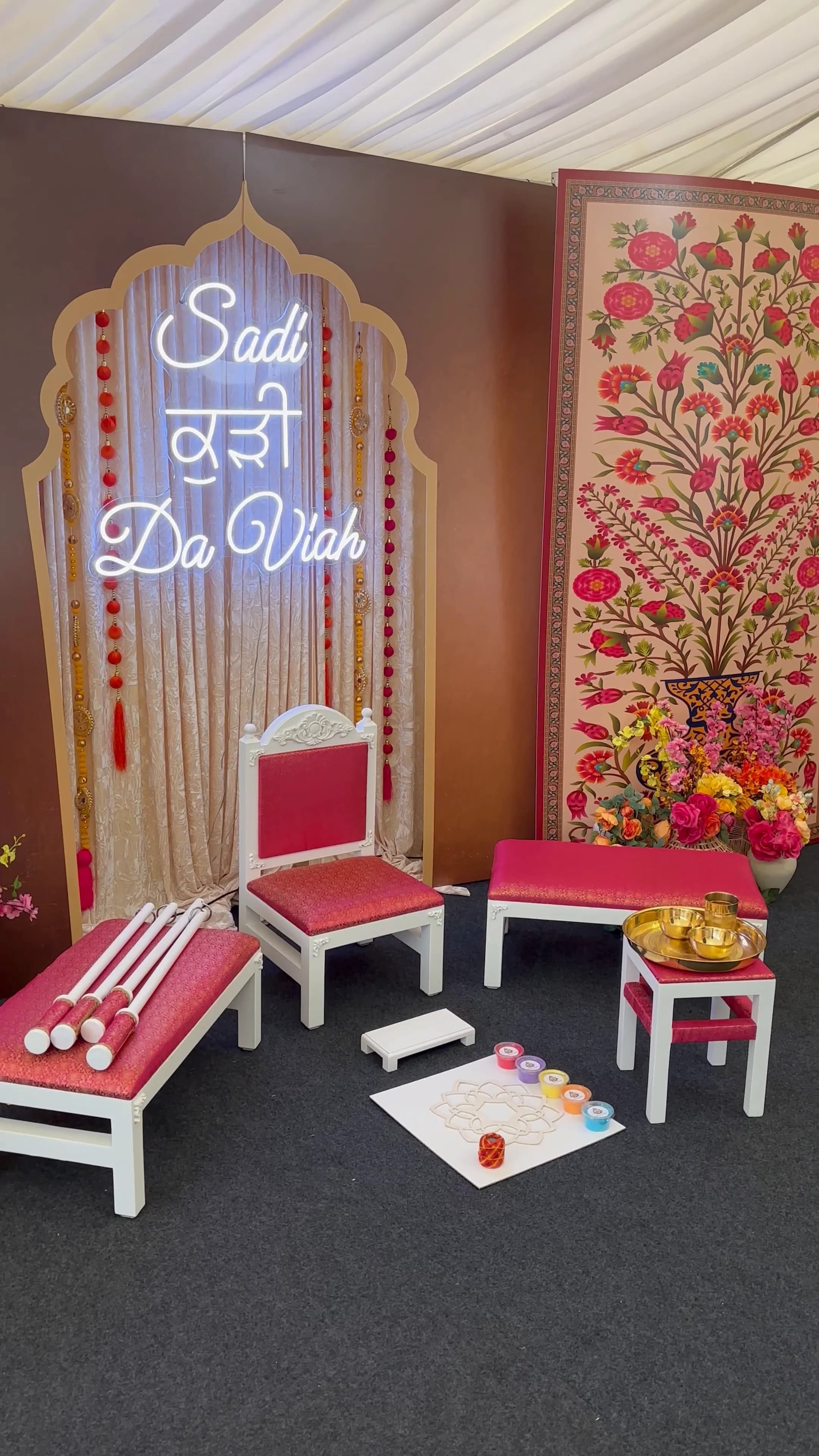 A complete Amaya Chairs Maiyan setting: the head chair and side benches, the tray table laid with the Sagan tray, chunni sticks, the Phatti and a rangoli board, beneath a neon Sadi Kuri Da Viah sign.