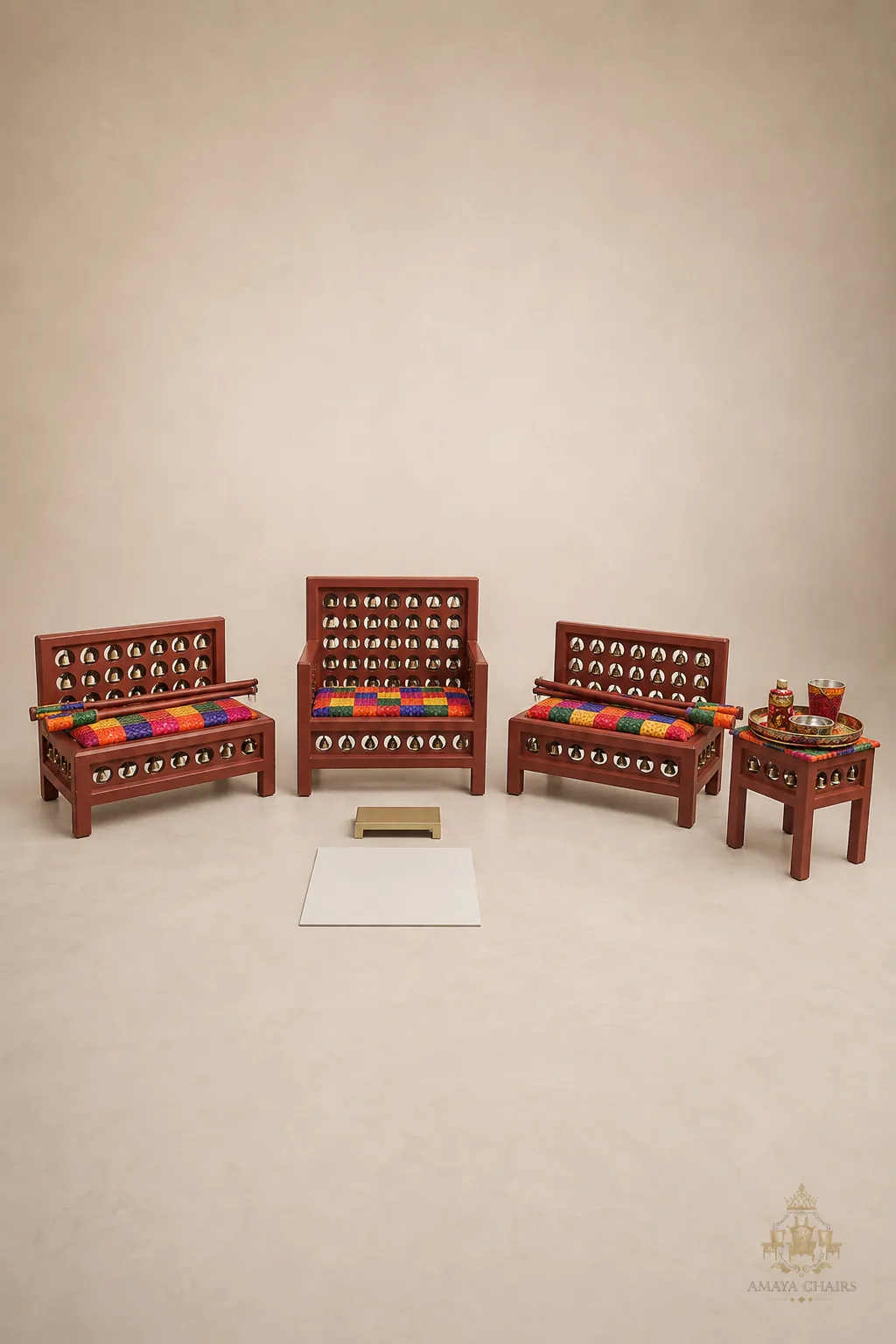 The Satrang Maiyan suite on an ivory backdrop: terracotta frames inset with rows of brass bells, seats upholstered in bright multicoloured phulkari-style blocks.