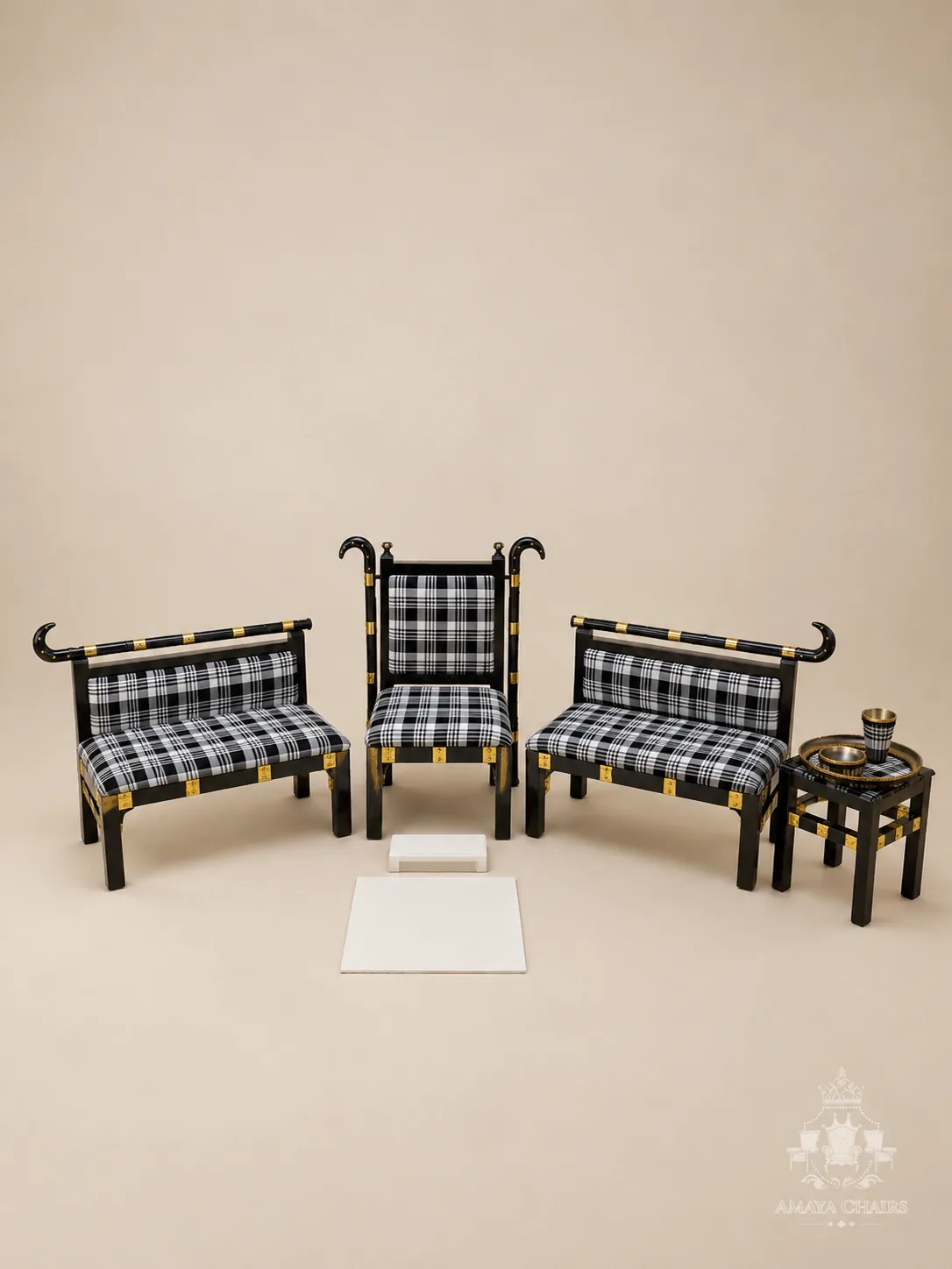 The Gabru Maiyan suite photographed on an ivory backdrop: a black lacquered head chair with curved gold finials flanked by two matching side benches in black-and-white check, with a tray table and brass Sagan tray.