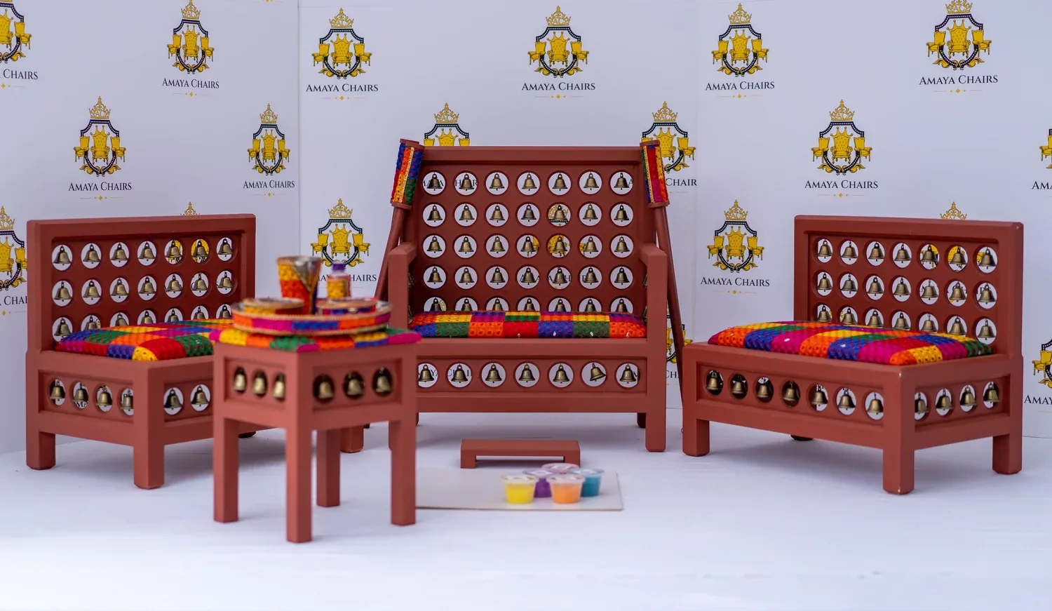 The Satrang suite photographed in full: terracotta frames inset with brass bells, seats worked in bright phulkari-style blocks.