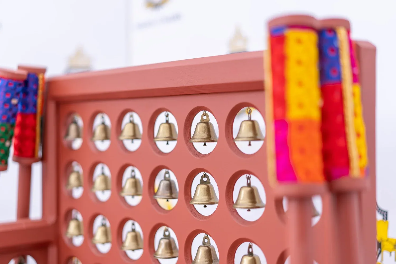 Close view of the rows of inset brass bells on a Satrang frame, beside a phulkari-style bolster.