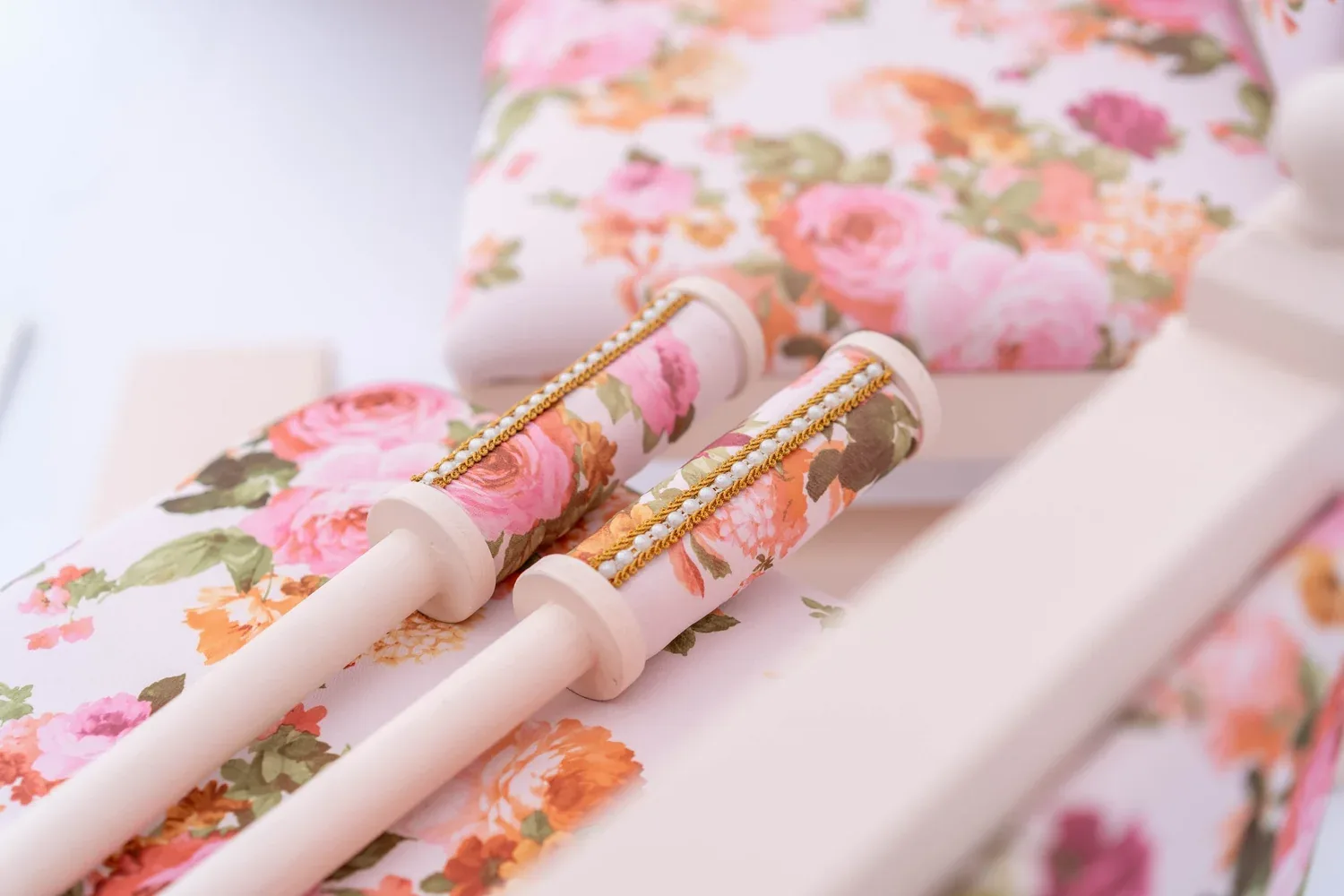 Close view of the Enchantress chunni sticks and rose print bolster resting on a carved ivory frame.
