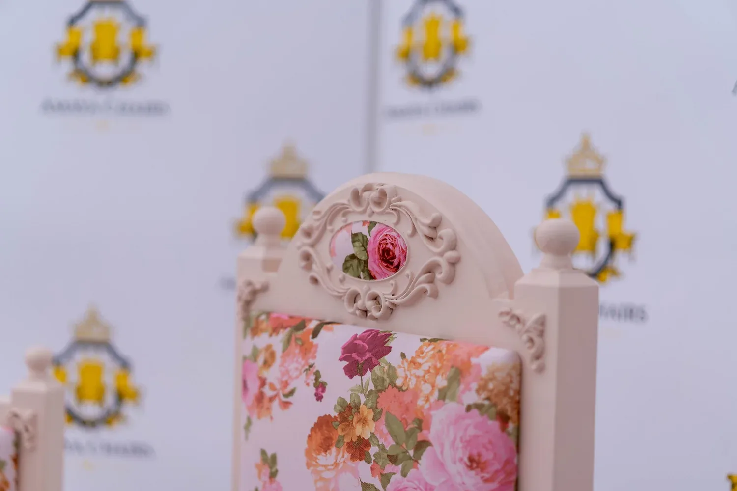 The Enchantress head chair photographed straight on, showing the carved cream crest and rose floral seat.